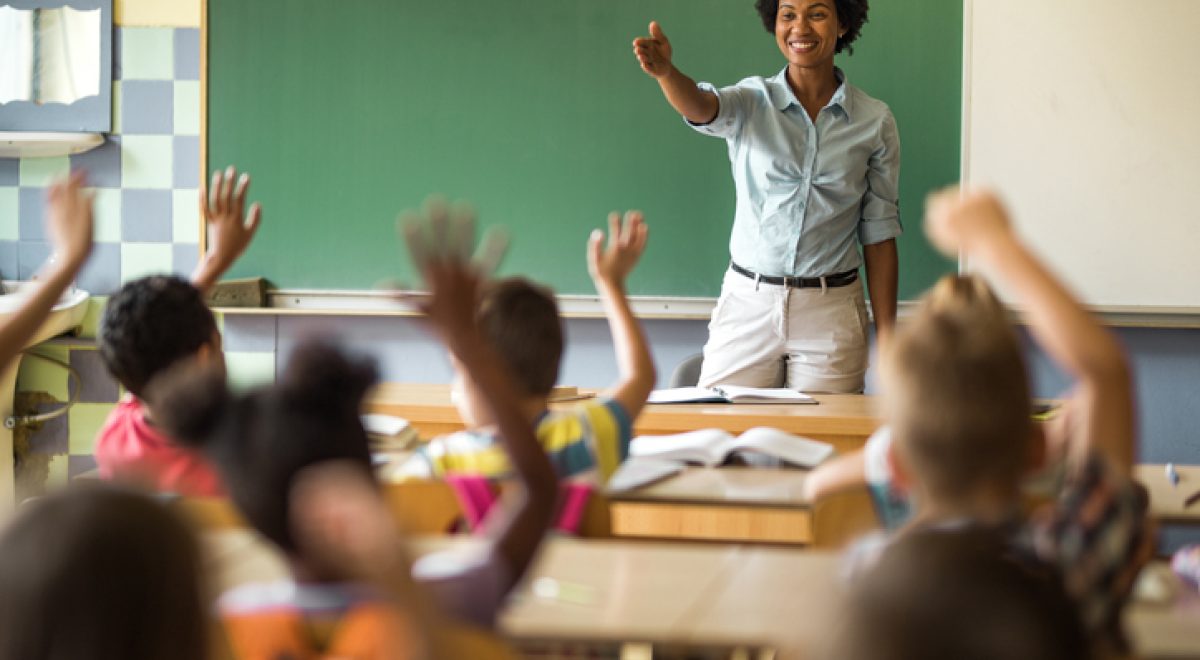 Happy black teacher aiming at school child to answer her question on a class at elementary school.